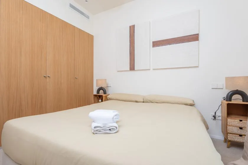 Un dormitorio con una cama grande, toallas dobladas y armarios de madera.