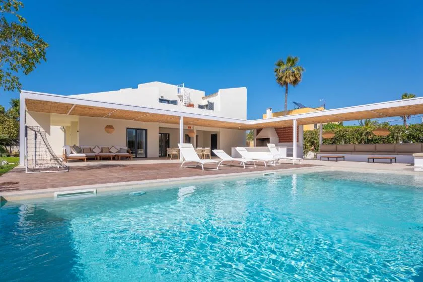 Piscina al aire libre junto a una casa moderna, con asientos en el patio.