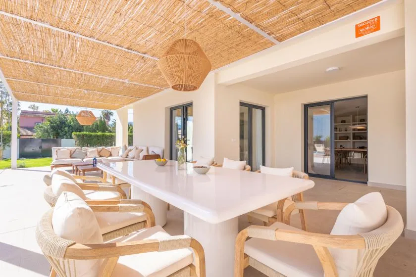 Un comedor exterior cubierto con una mesa larga y asientos tejidos.