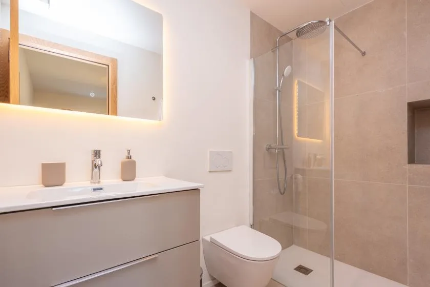 Un baño moderno con lavabo, espejo iluminado, inodoro y ducha de cristal.