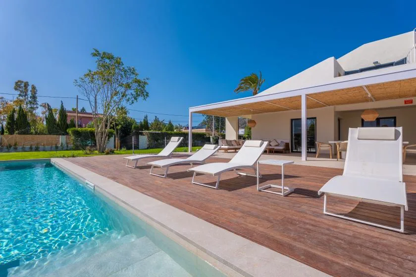 Una piscina al aire libre junto a una terraza de madera con asientos reclinables.