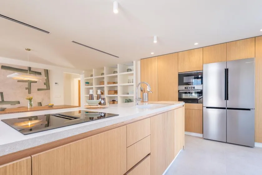 Una cocina moderna tiene una isla larga con placa de cocción y gabinetes de madera clara.