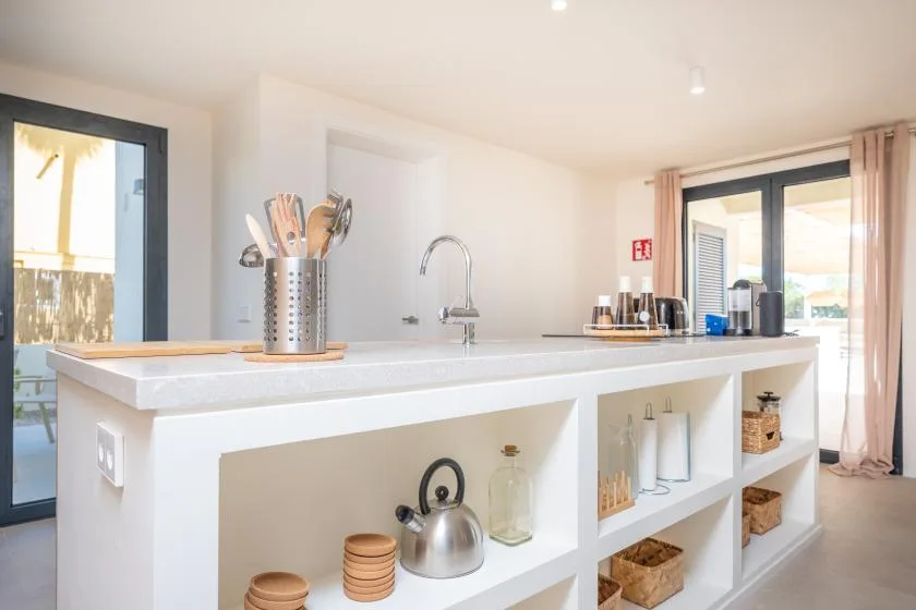 Una cocina luminosa con una isla blanca y estantes abiertos.
