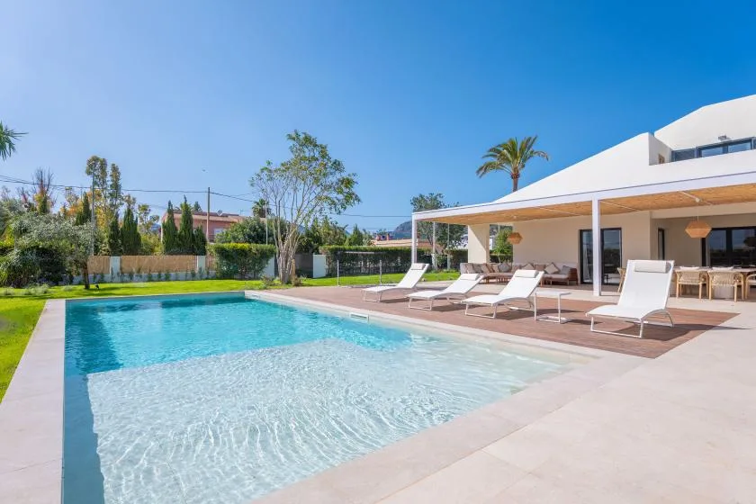 Una piscina junto a una casa moderna, con tumbonas en el patio.