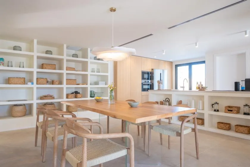 Un comedor luminoso con una mesa de madera, asientos y estantes abiertos.