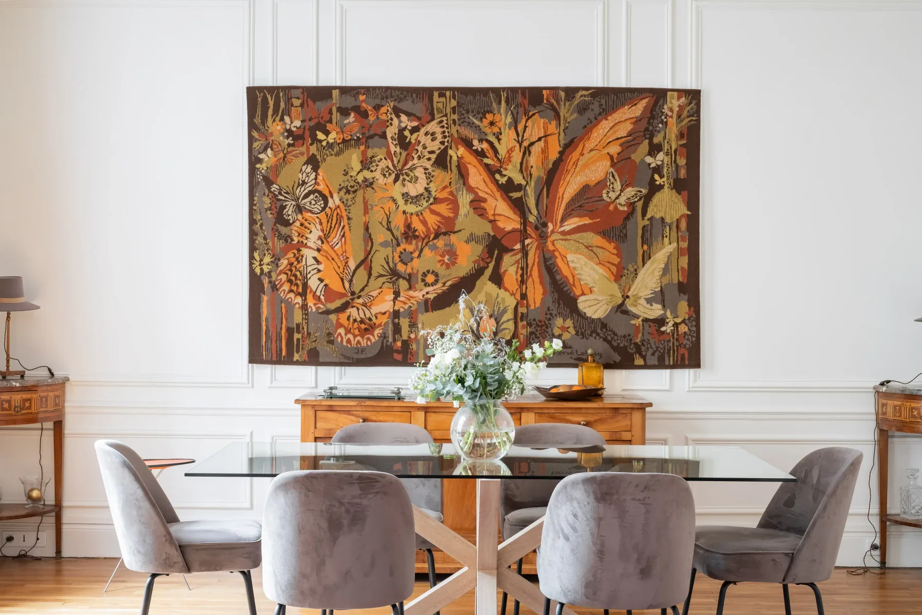 Dining area with a glass table and large butterfly artwork on the wall.