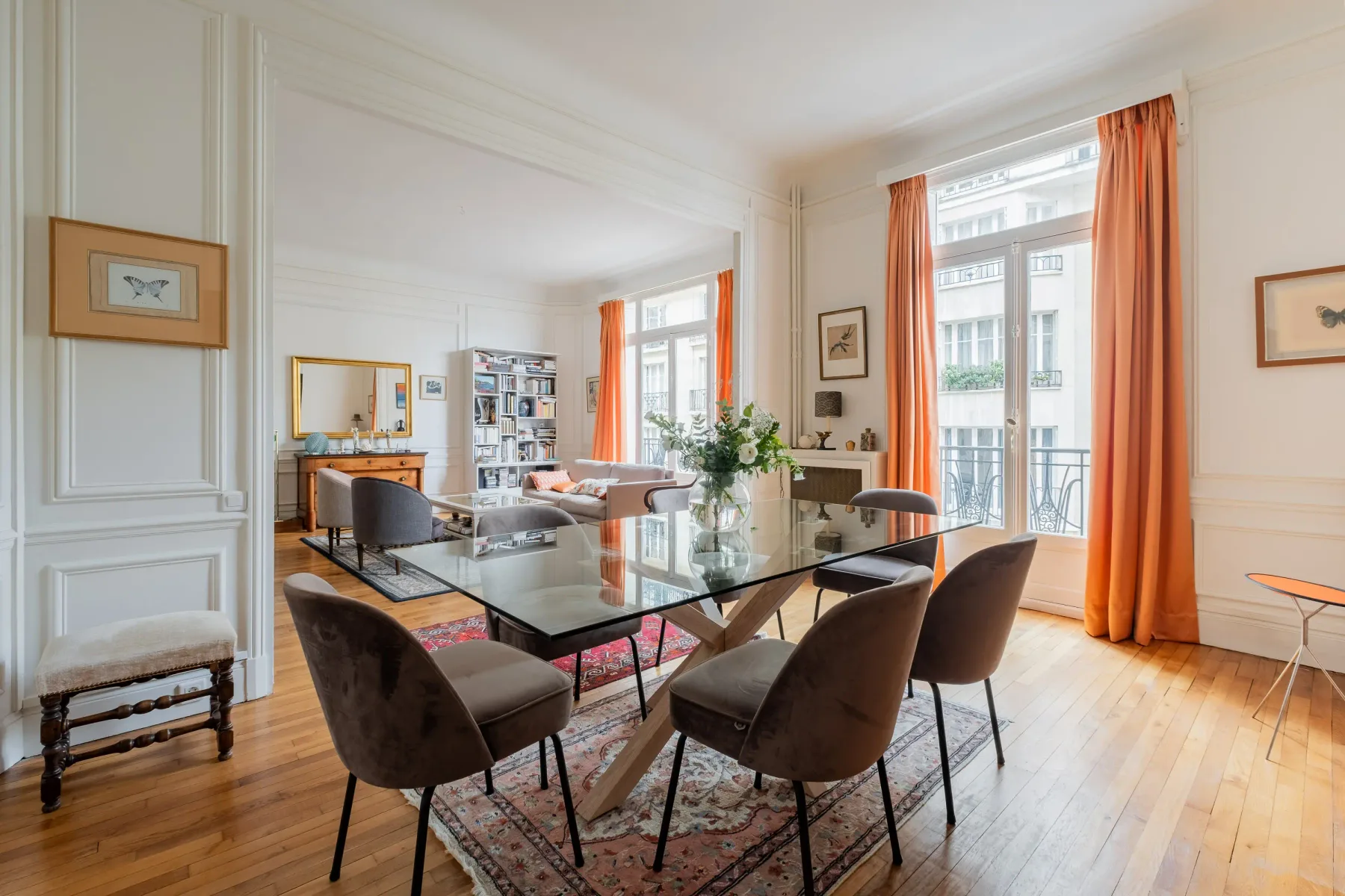 A bright dining and living room with a glass dining table and orange curtains.