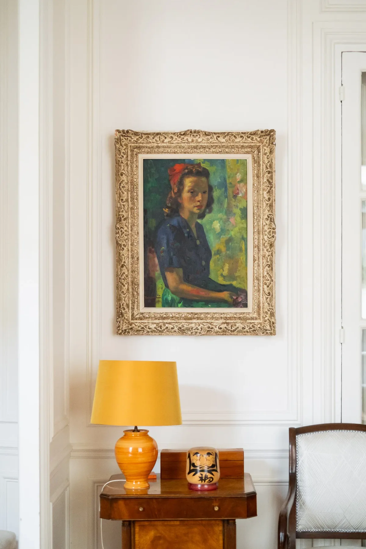 A framed portrait hangs above a wooden table with a lamp.