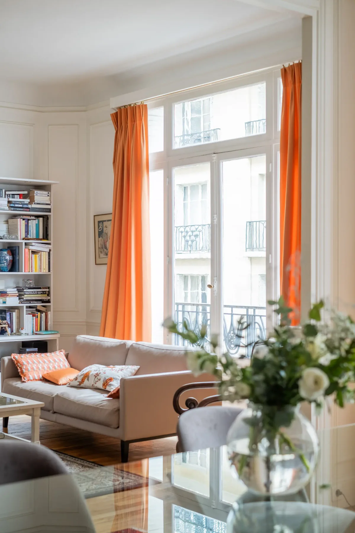 A bright living room with seating beside large windows and orange curtains.