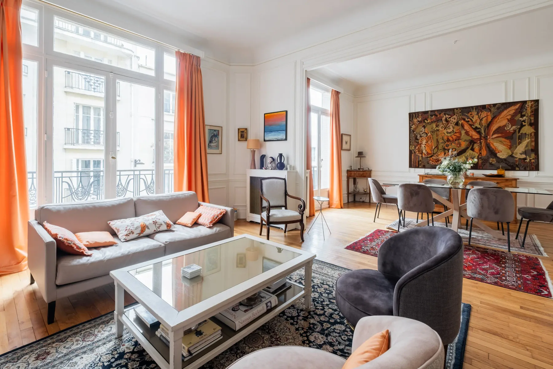 A bright living room with seating beside large windows and a dining area.