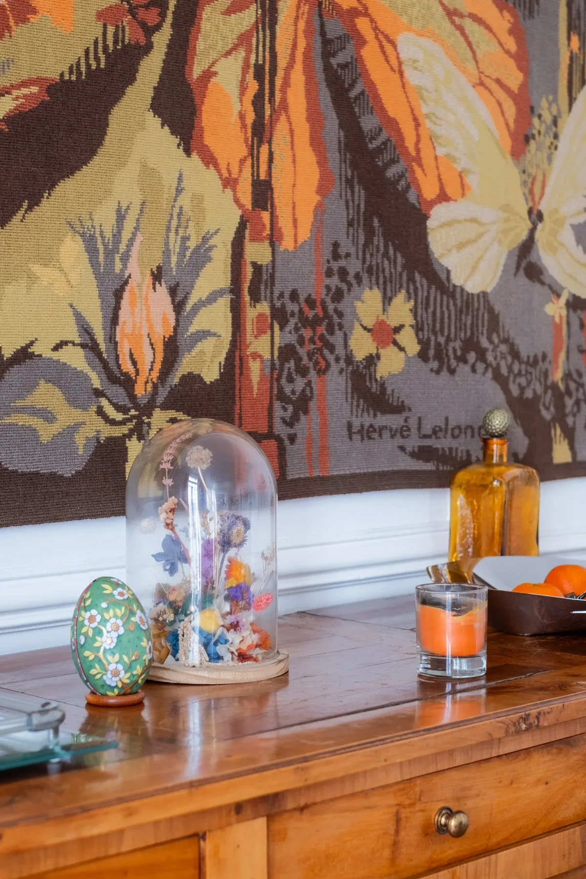 A wooden sideboard displays decorative objects beneath a colorful butterfly tapestry.