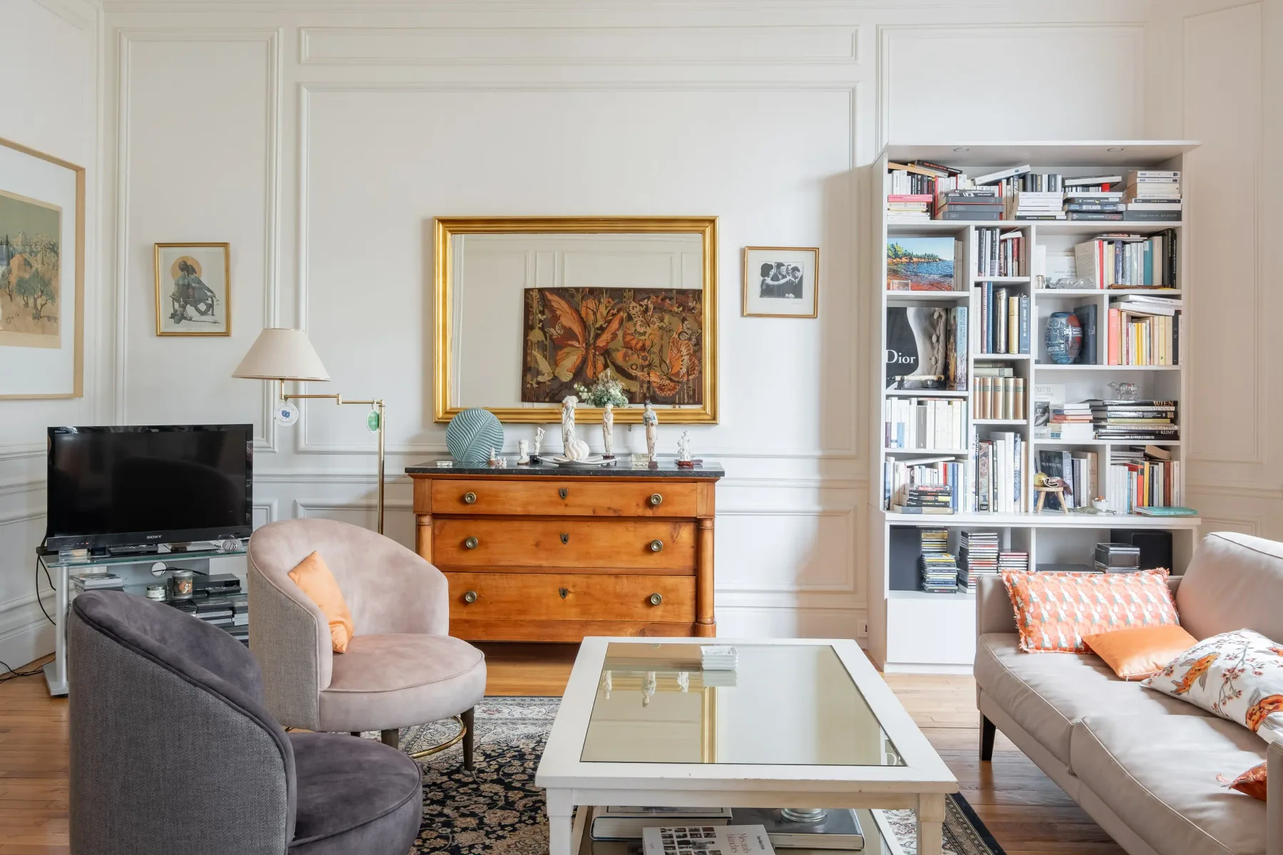 A living room with seating, a glass coffee table, and a tall bookshelf.