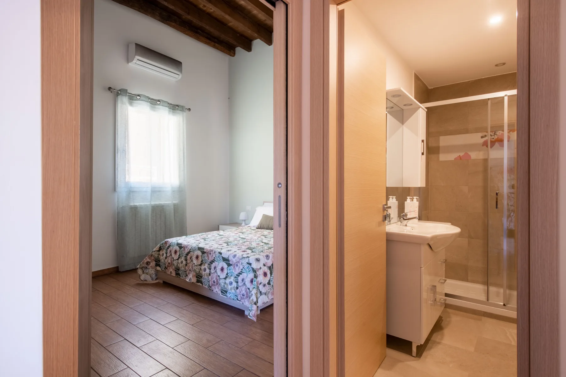 Se ve un dormitorio con una cama estampada junto a un baño con lavabo y ducha.