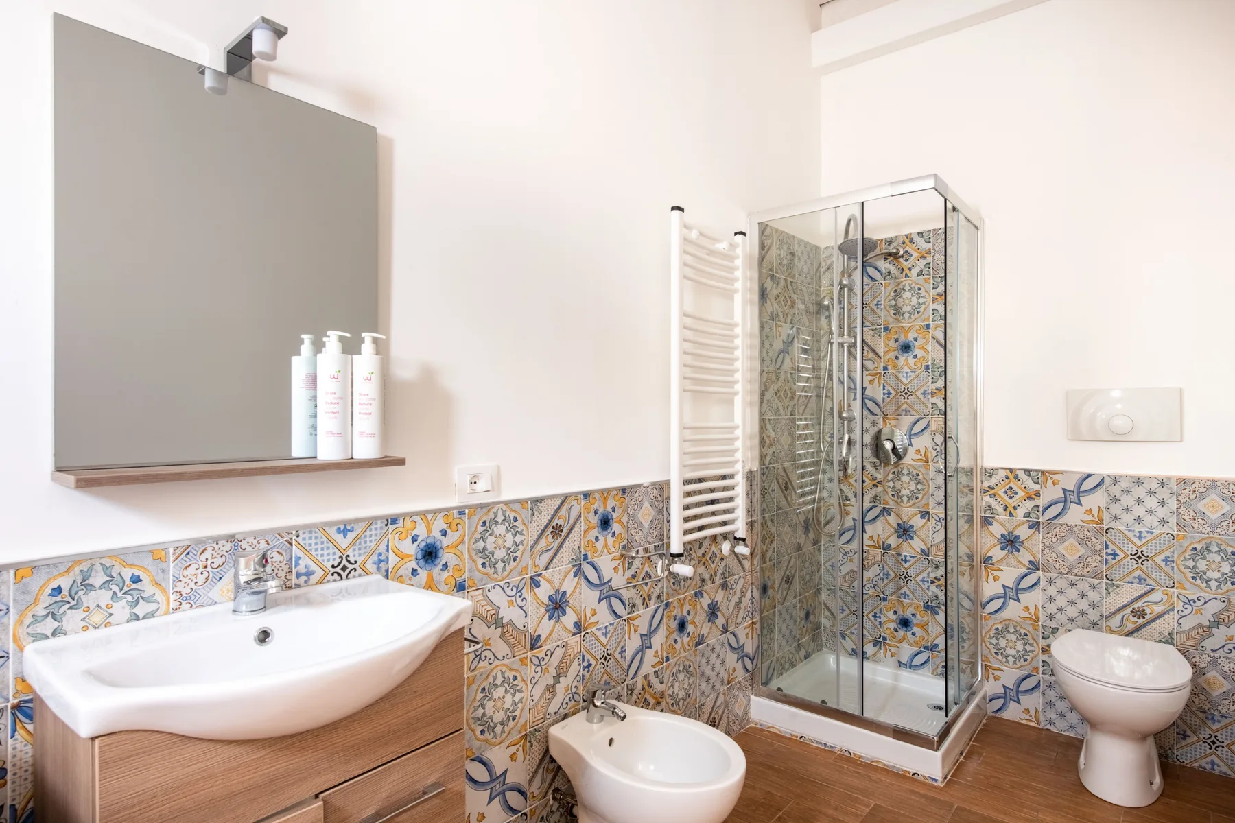 Un baño luminoso con lavabo, azulejos estampados y una ducha de vidrio.
