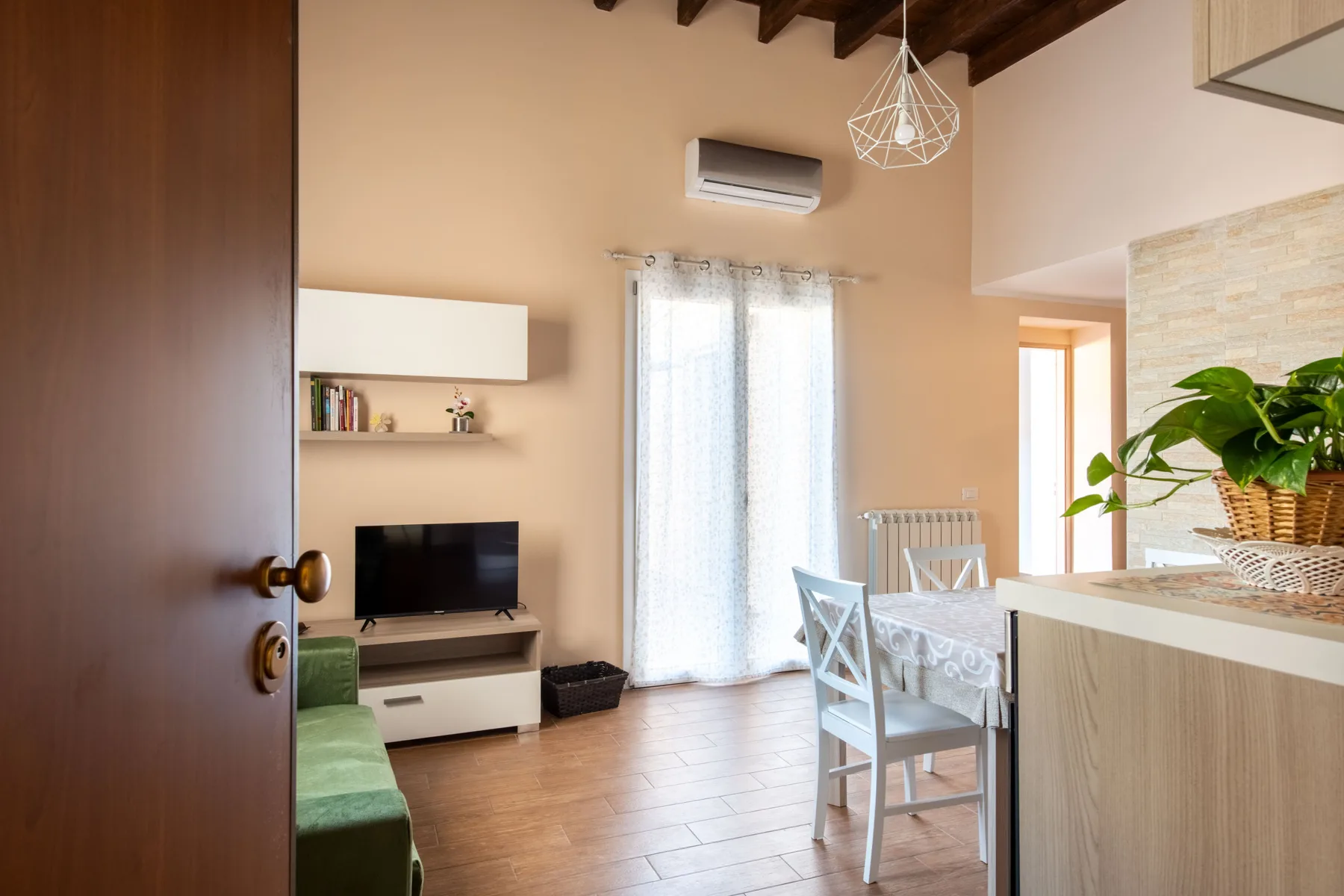 Una luminosa sala de estar y comedor tiene un televisor, una mesa y una amplia ventana con cortinas.