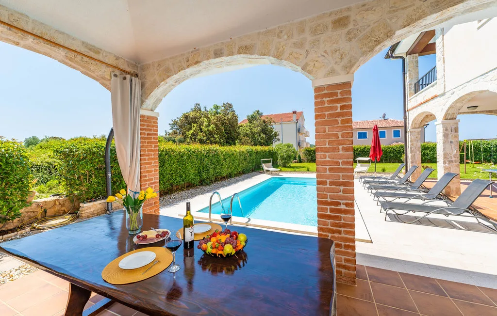 A shaded patio overlooks a swimming pool, with loungers beside the water.
