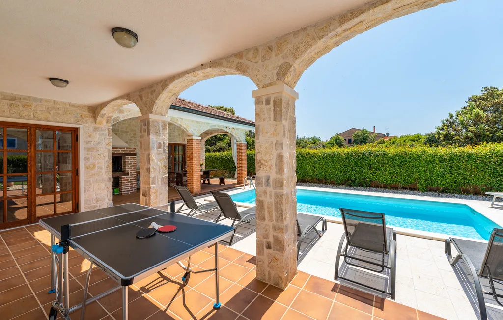 A covered patio with a table tennis table opens onto a swimming pool.