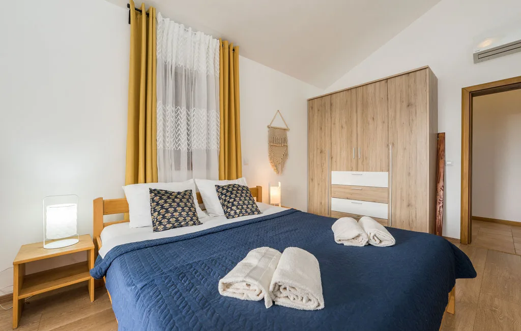 A bedroom with a large bed dressed in navy bedding and yellow curtains.