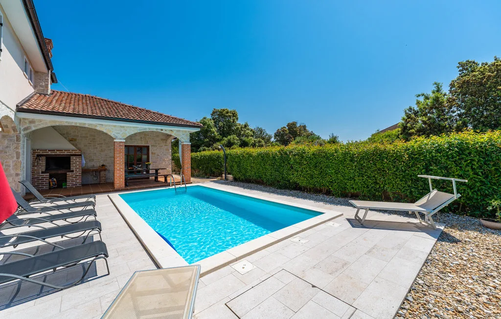 An outdoor swimming pool sits beside a paved patio with lounge chairs and greenery.