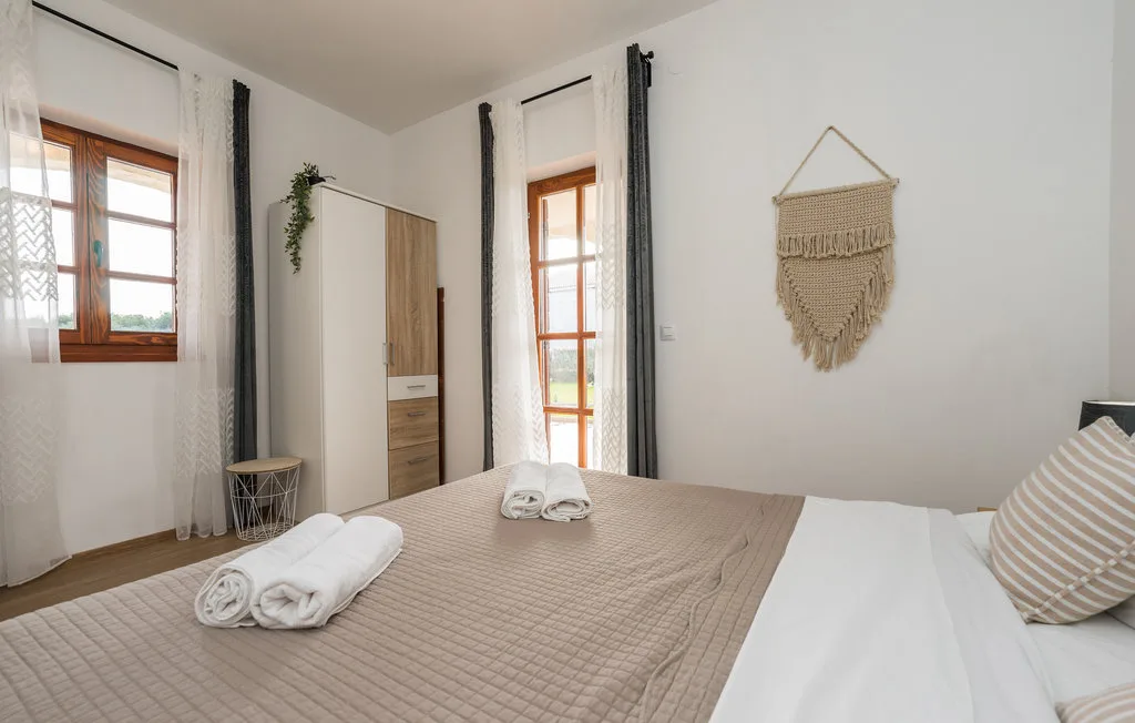 A bedroom with a neatly made bed, wooden-framed windows, and dark curtains.
