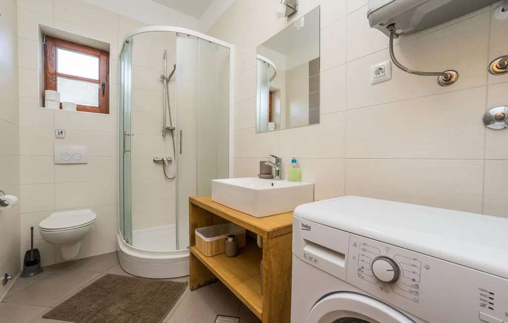 A tiled bathroom with a shower, sink, toilet, and washing machine.