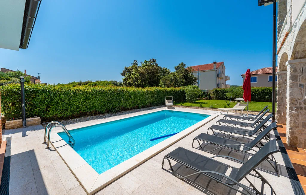 An outdoor swimming pool is surrounded by lounge seating and a green hedge.
