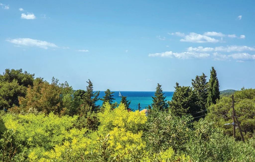 A coastal landscape with blue sea visible beyond green trees and shrubs.
