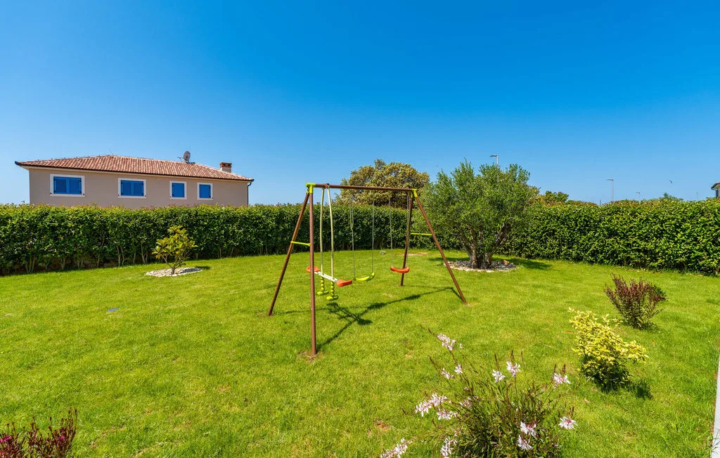 A grassy garden with a metal swing set and hedges in the background.