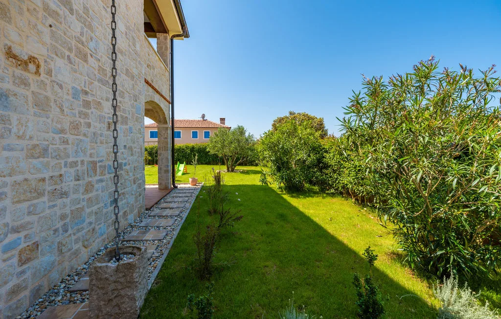 A grassy garden beside a stone building, with shrubs and trees.