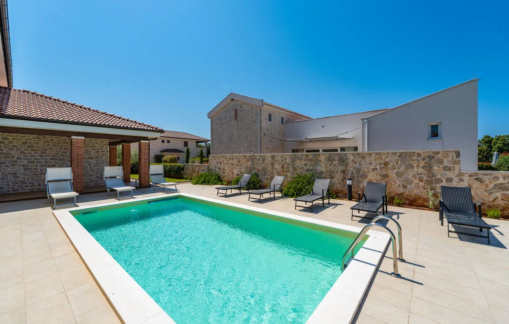 An outdoor swimming pool beside a stone wall and patio seating.