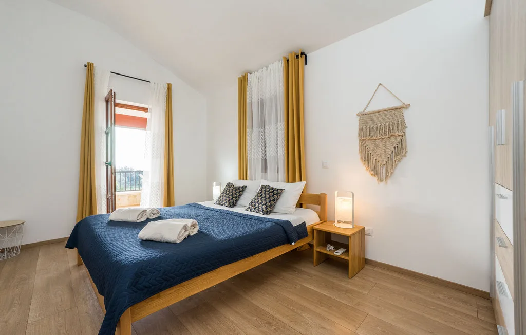 A bedroom with a bed covered in navy bedding and mustard curtains.