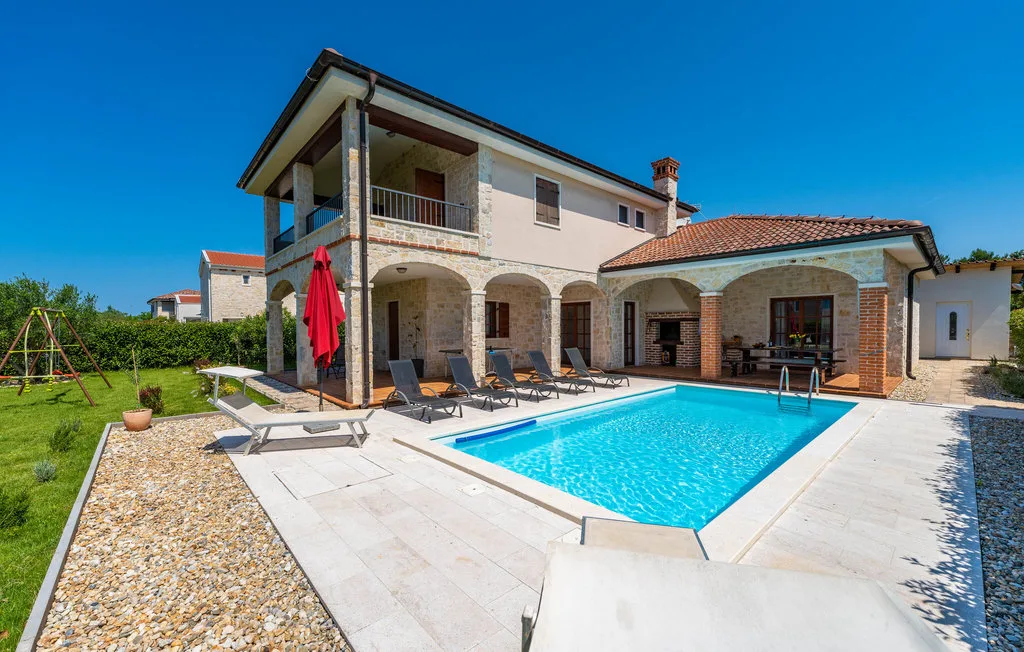 A two-story house overlooks a swimming pool, with lounge seating on the paved patio.