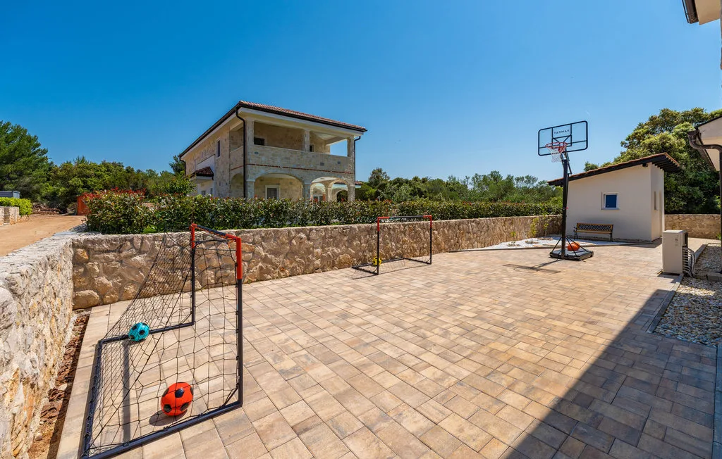 An outdoor paved recreation area has small soccer goals and a basketball hoop.