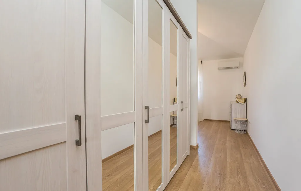 A bright hallway with mirrored closet doors and wood flooring.