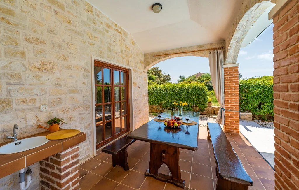 A covered outdoor dining area with a long wooden table beside the garden.