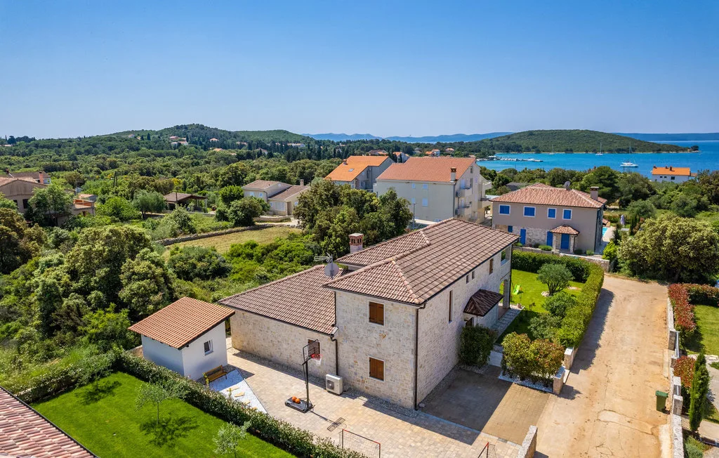 Aerial view of stone houses and gardens with the blue sea in the distance.