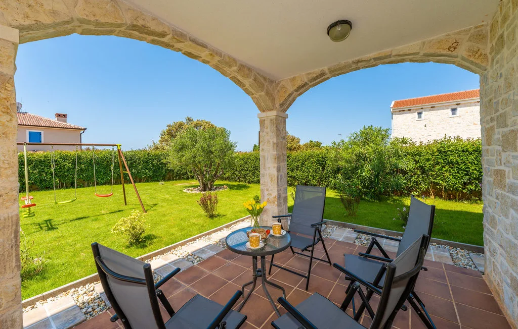 A covered patio with outdoor seating overlooks a green garden and play swing.