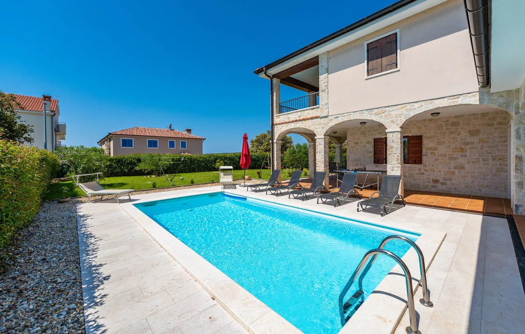 A swimming pool beside a two-story house with covered patio seating.