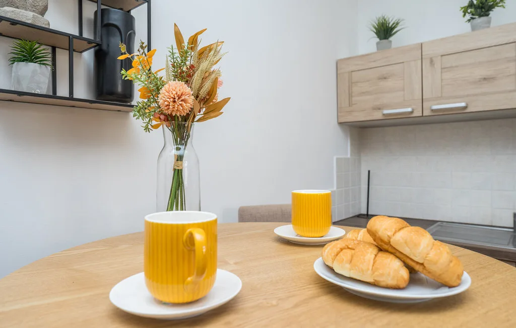 A kitchen counter with pastries and yellow mugs on a wooden table.
