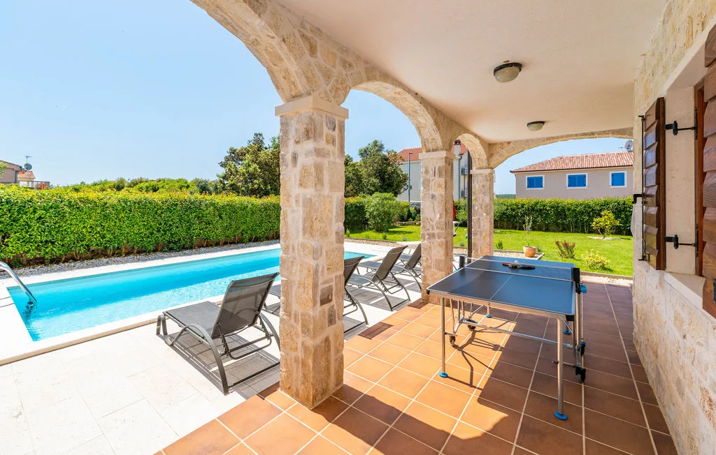 A covered patio overlooks a swimming pool, with outdoor seating and a table tennis table.