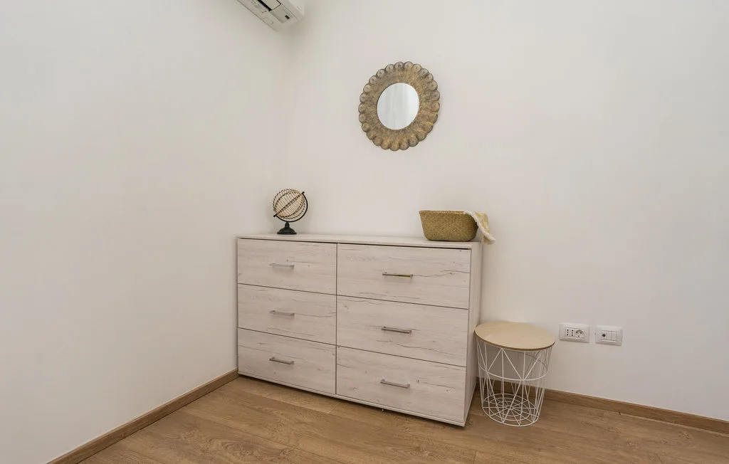 A bedroom corner features a light-colored dresser and a small side table.