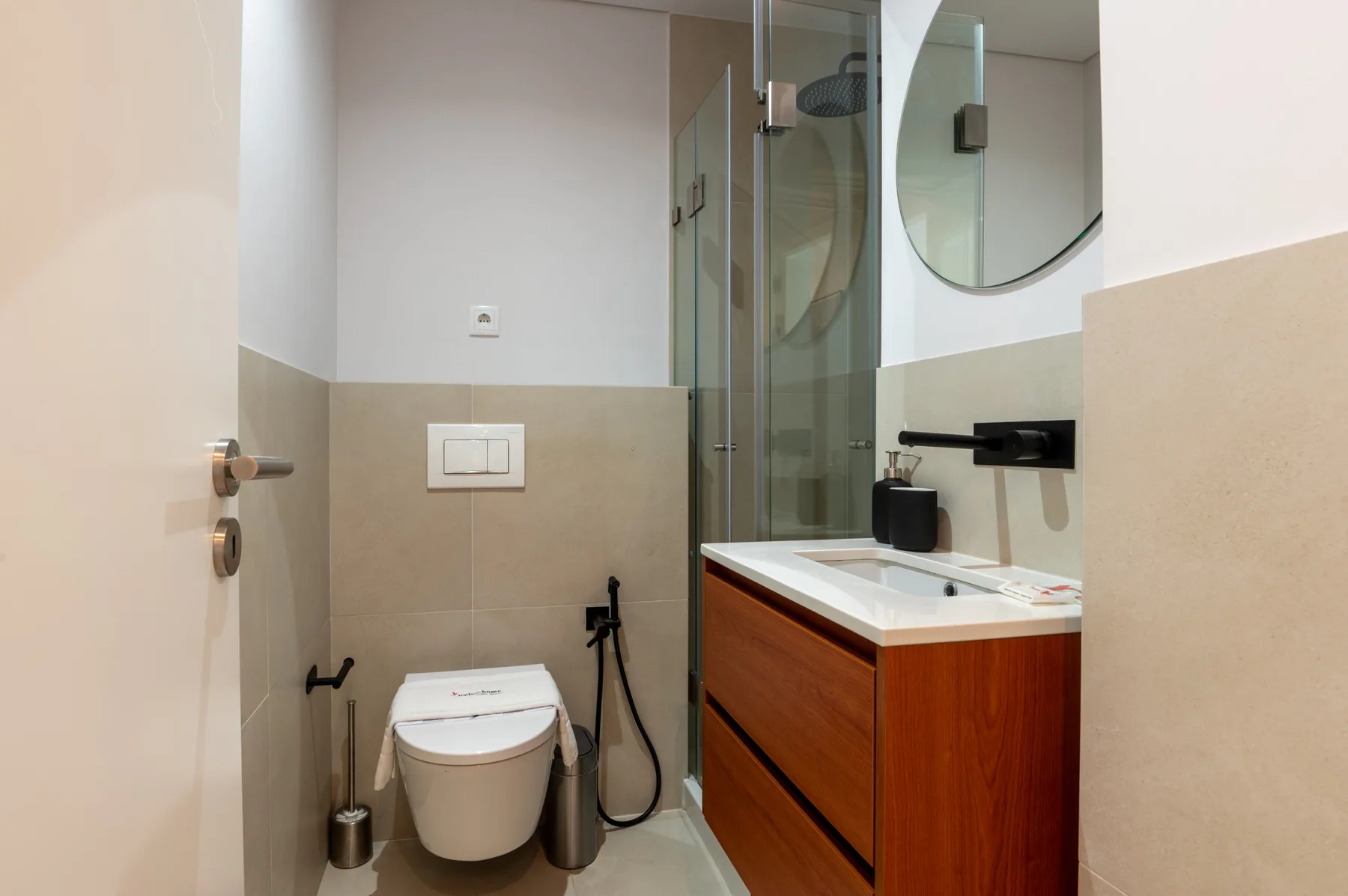 A modern bathroom with a toilet, glass shower, and wood-toned vanity.