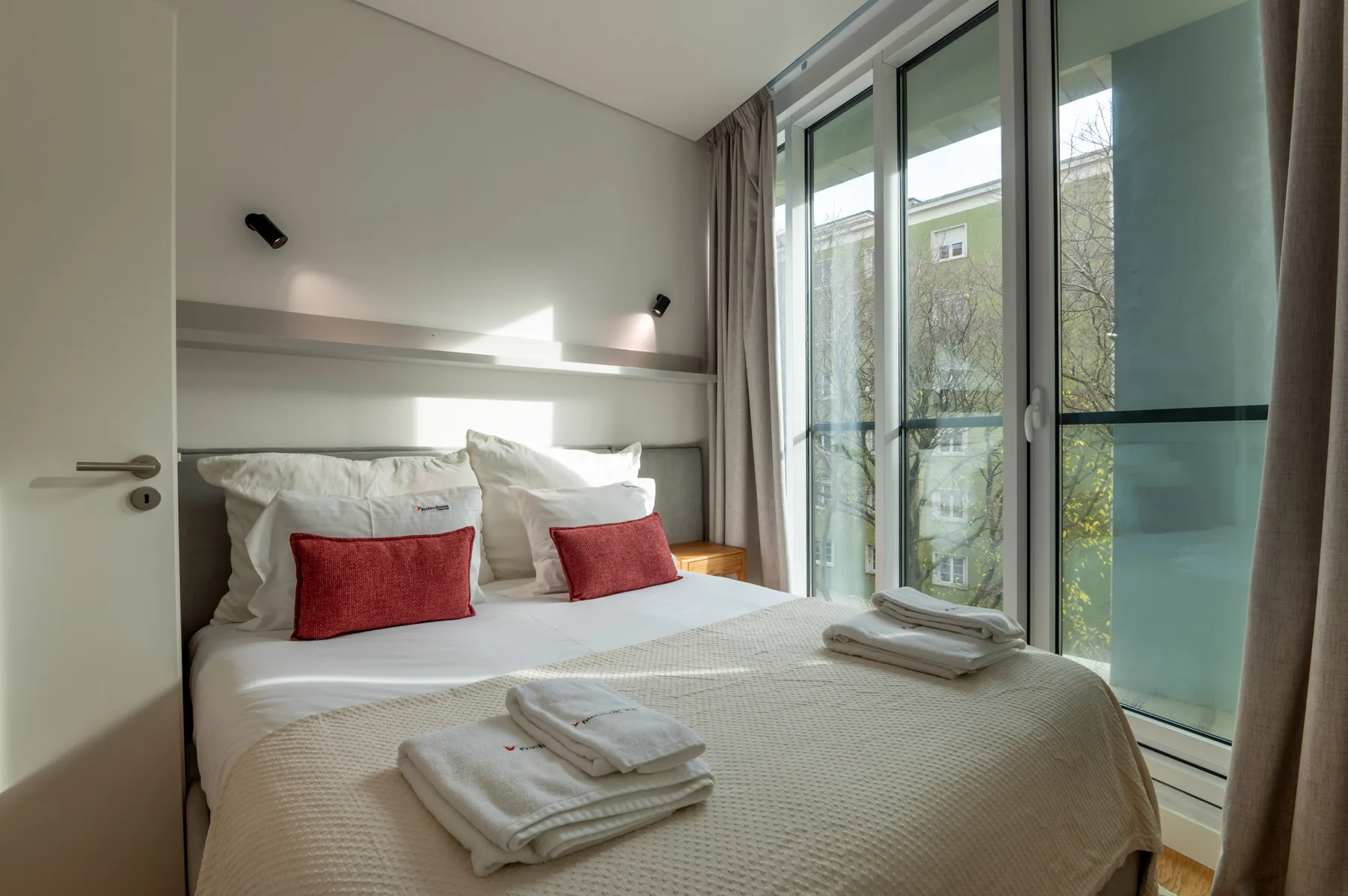 A bedroom with a neatly made bed beside large windows.