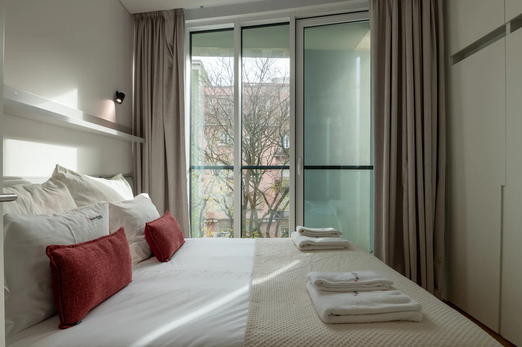 A bright bedroom with a neatly made bed and folded towels.