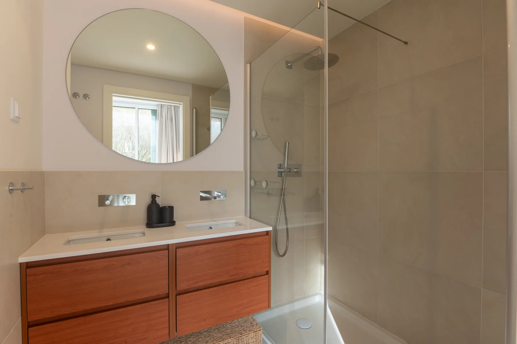 Bathroom with a wood-toned vanity, round mirror, and glass shower.