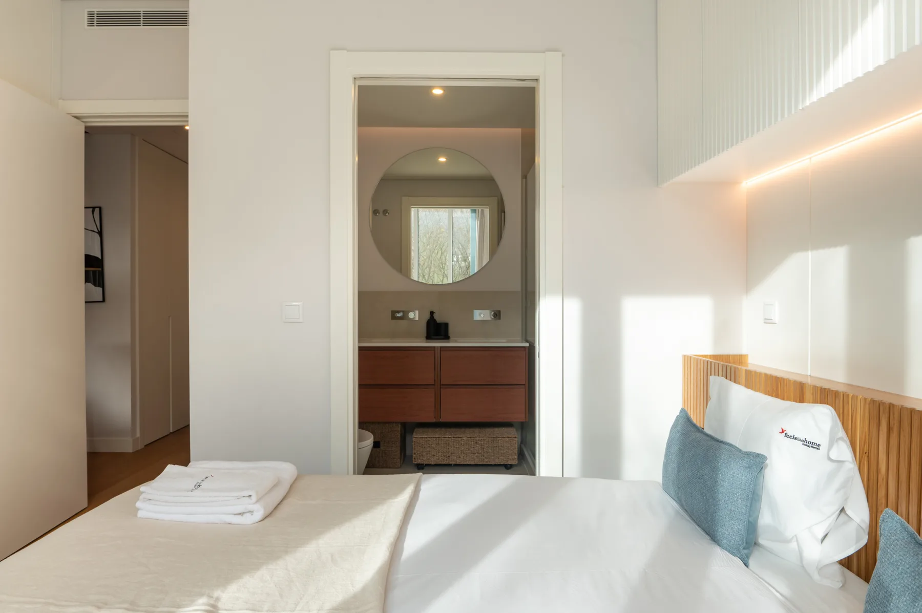 A bright bedroom with a bed and an open doorway to a vanity area.