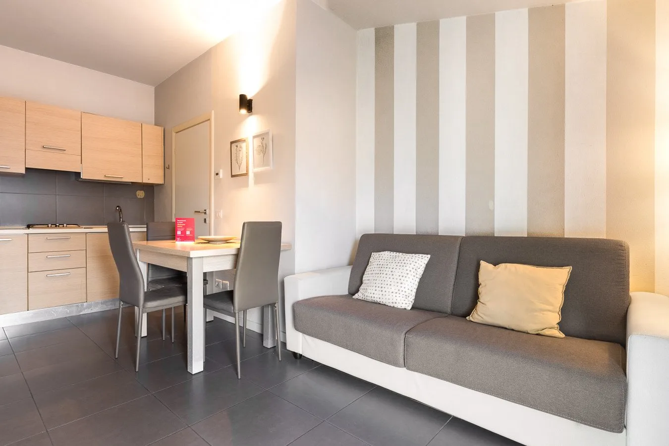 Una sala de estar con un sofá gris junto a una cocina compacta y una mesa de comedor.