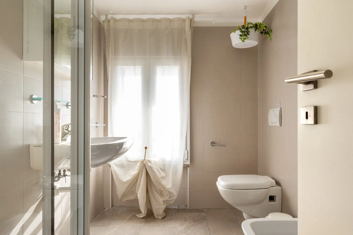 Un baño luminoso con azulejos, ducha de vidrio, lavabo e inodoro.