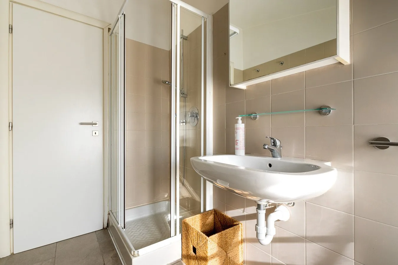 Un baño alicatado con ducha de cristal, espejo de pared y lavabo blanco.