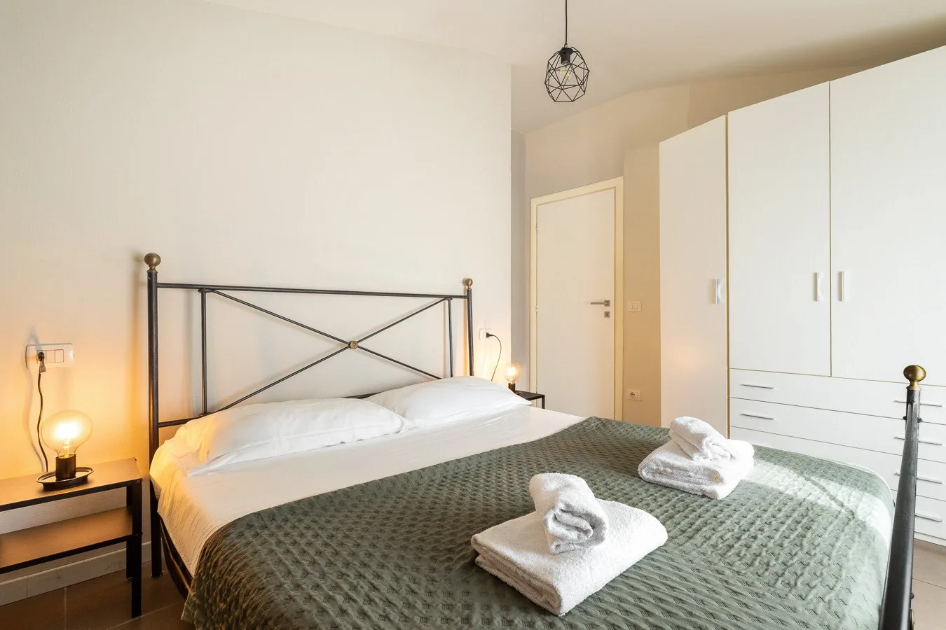 Un dormitorio con una cama doble, toallas dobladas y un armario blanco alto.